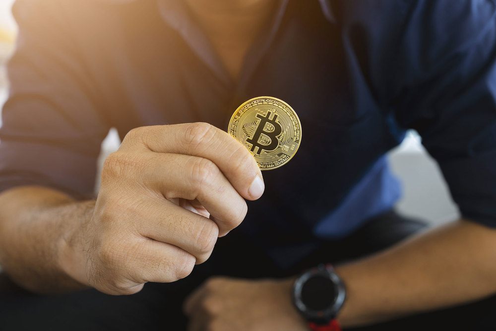 Man in blue shirt holding bitcoin
