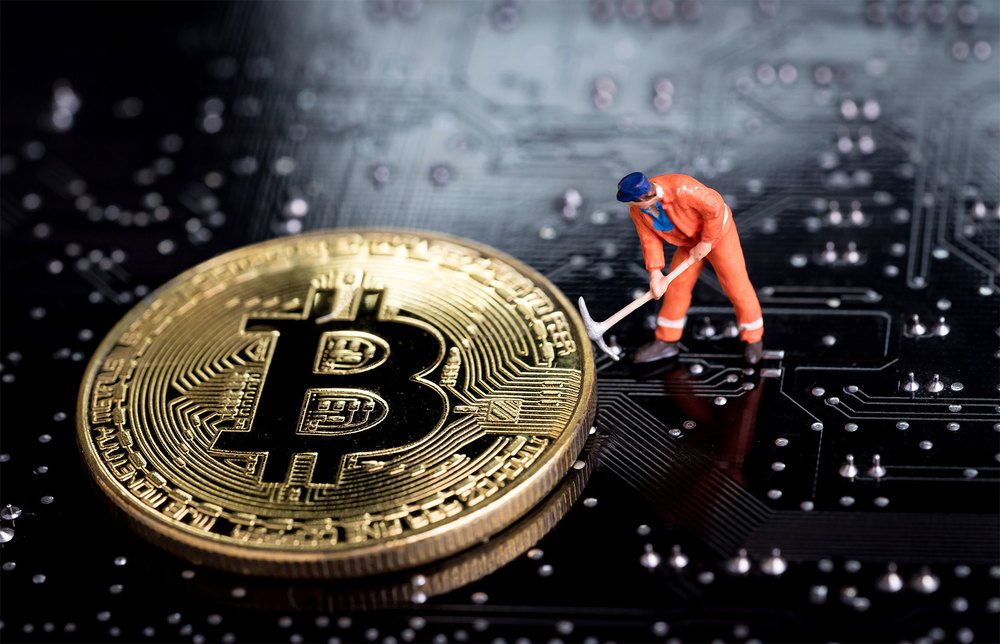 Miniature worker holding mattock beside Bitcoin on top of circuit board