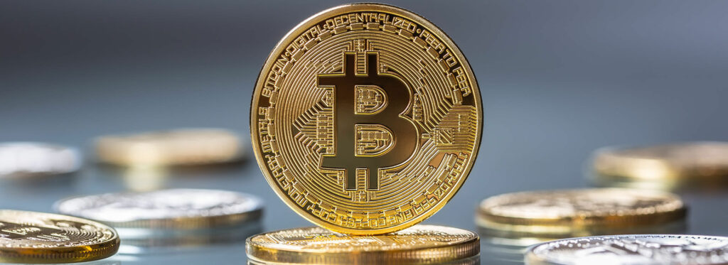 Gold bitcoin surrounded by gold and silver coins on gray table