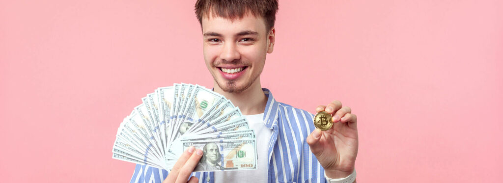 Man smiling holding bitcoin and and fan of cash on pink background